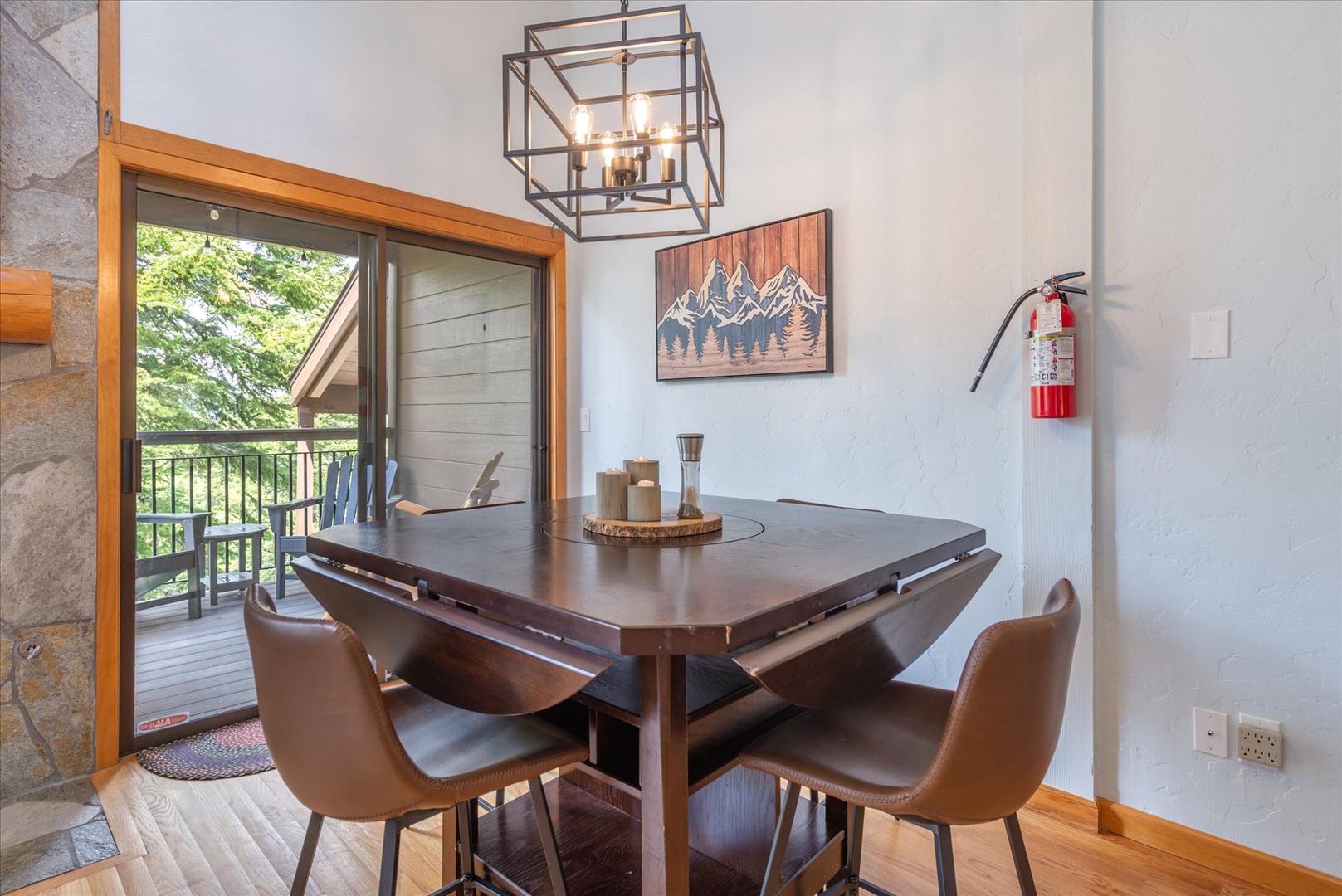 Your modern dining area opens to a private balcony with peaceful forest views, where you can savor meals beneath a statement chandelier and rustic mountain artwork.