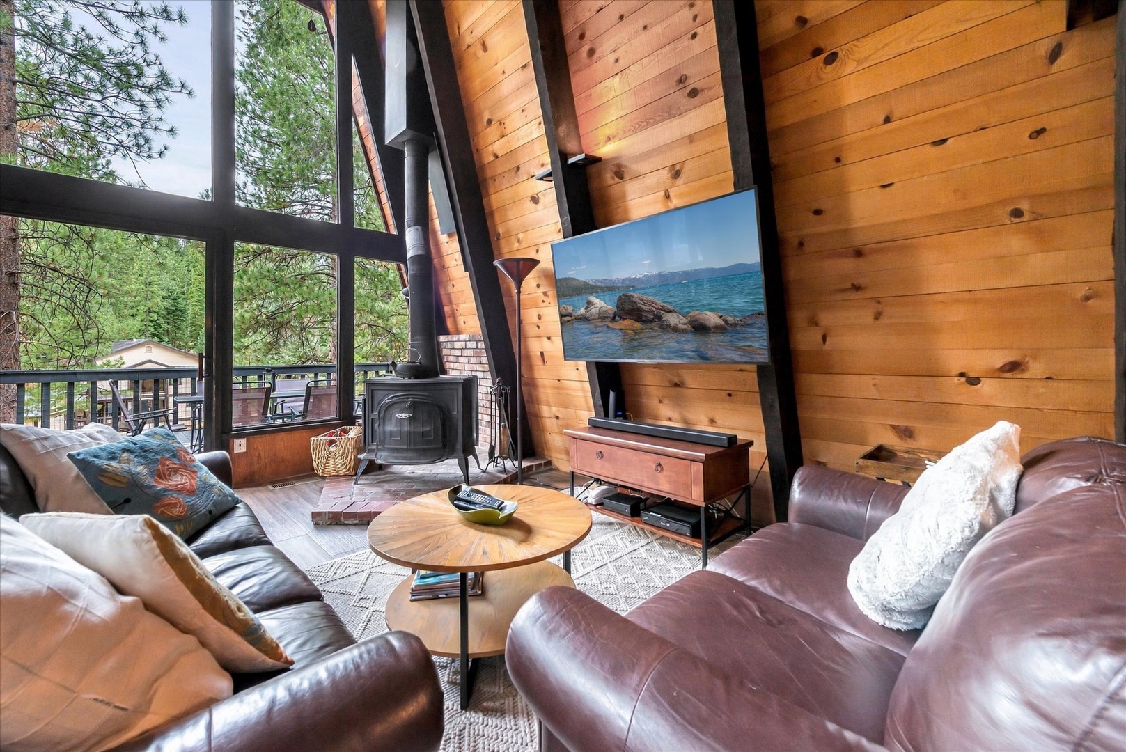 Unwind in your welcoming living room with soaring cathedral ceilings, plush leather sofas, and a cozy wood-burning fireplace. Floor-to-ceiling windows frame stunning forest views right outside.
