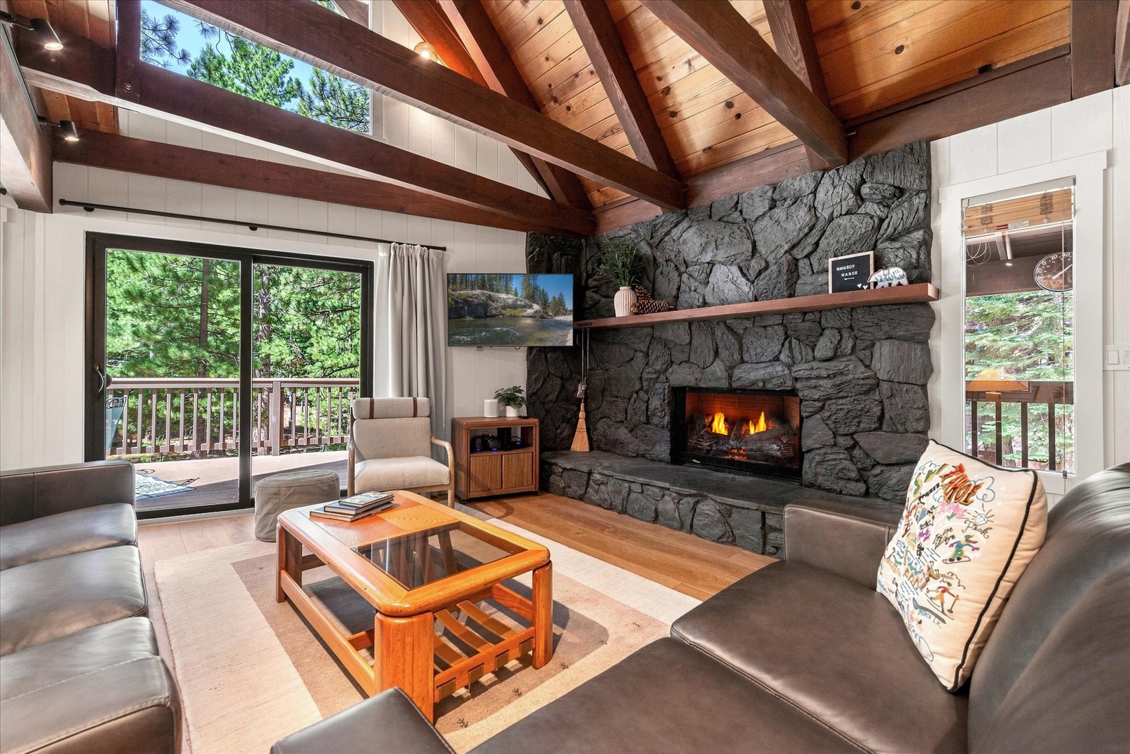 : Curl up by the crackling stone fireplace and soak in forest views from your private balcony through soaring windows in this cozy, sun-drenched living room with stunning vaulted ceilings.