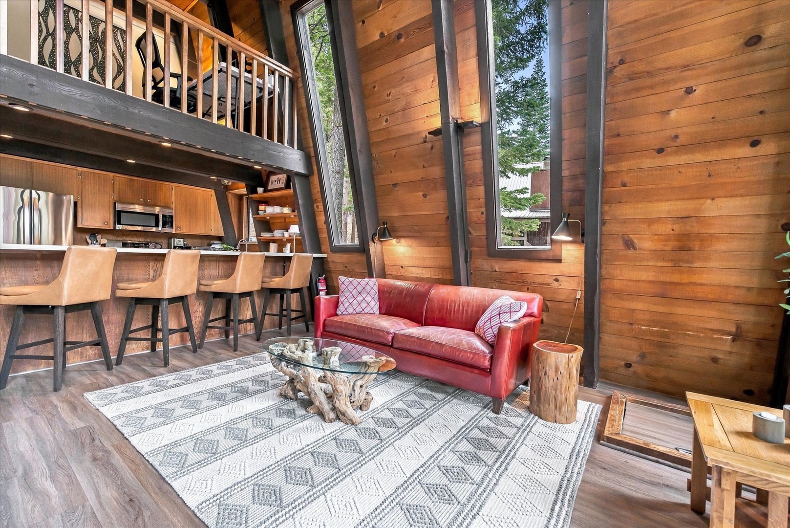 Relax in your open-concept retreat where soaring ceilings, warm wood walls, and tall windows frame the forest beyond. Curl up on the leather sofa or gather at the breakfast bar—this inviting space blends rustic charm with modern comfort.