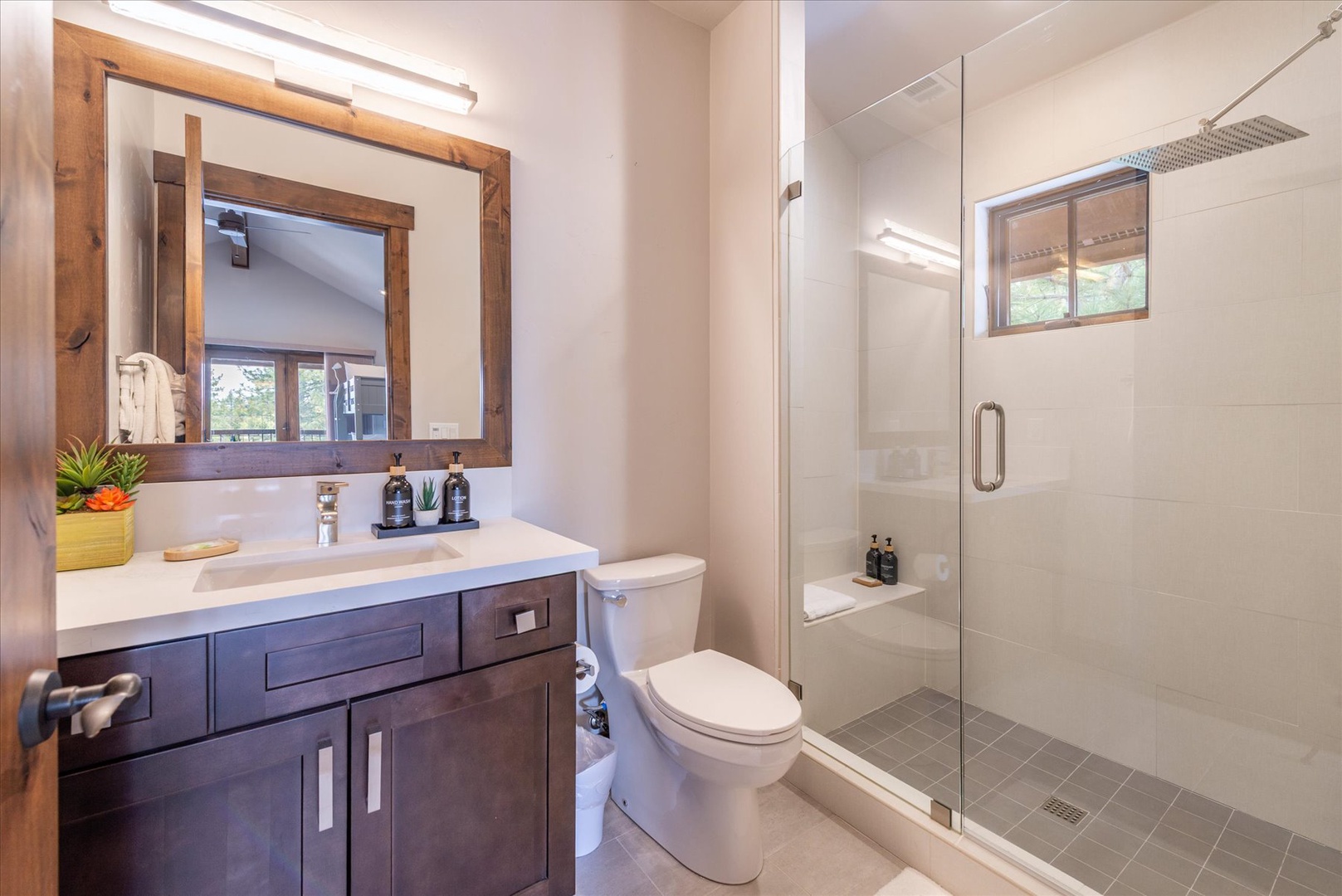 Refresh in your modern ensuite bathroom featuring elegant wood vanity, spacious glass shower, and thoughtful amenities for a perfect start to your day.