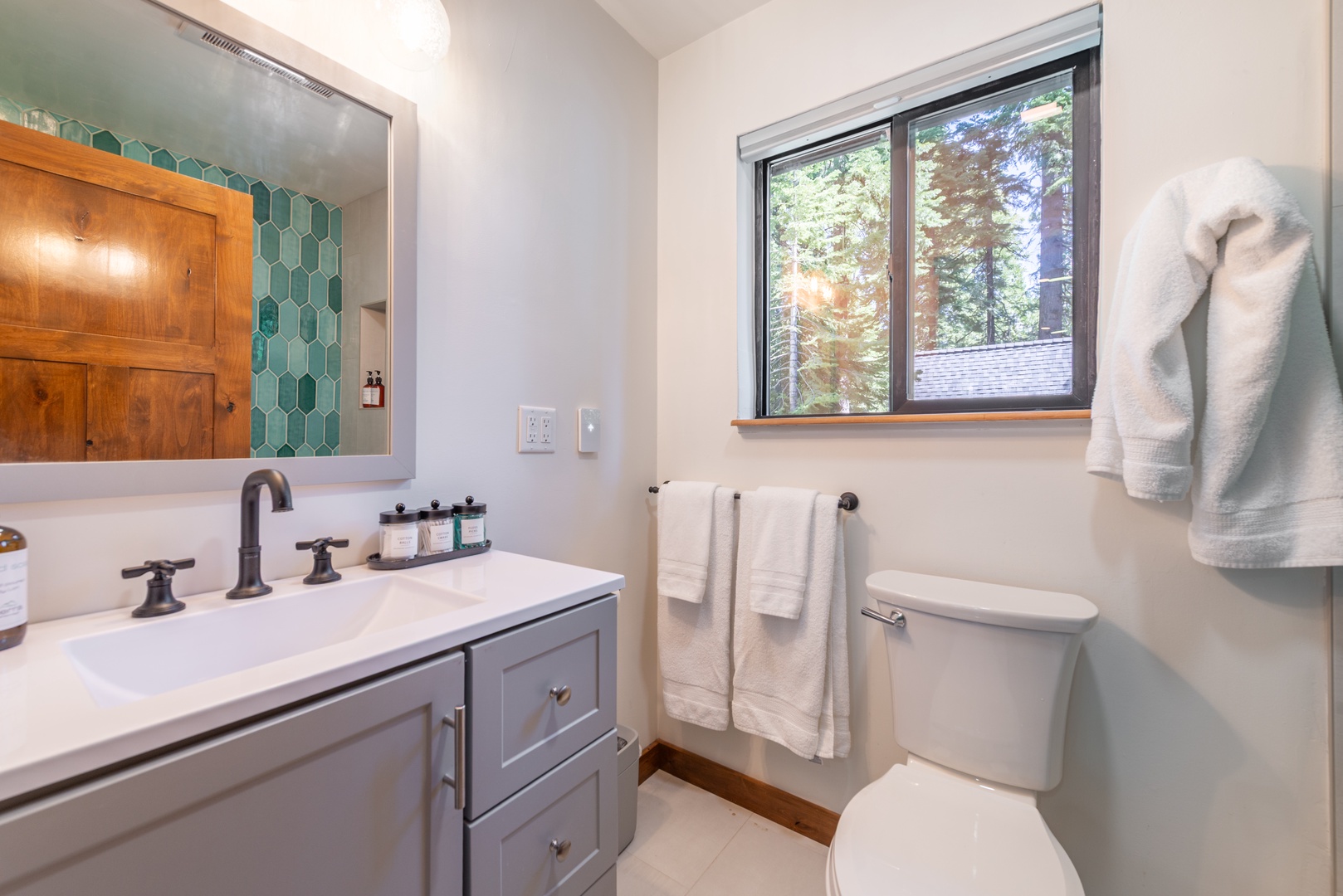 Step into your bright upstairs bathroom with fresh towels, a chic vanity, and a charming view of tall trees framed by the window—perfect for refreshing after a day of adventure.