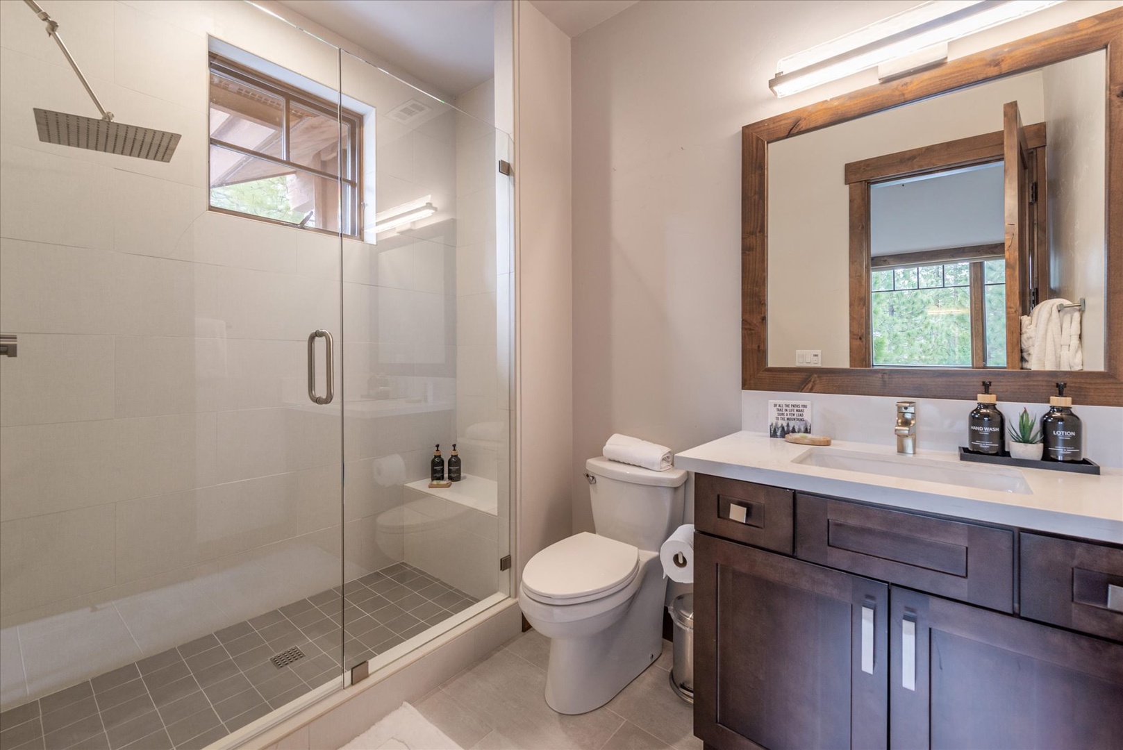 Step into your spacious ensuite bathroom featuring a sleek walk-in shower and elegant wood vanity with premium amenities for your comfort.