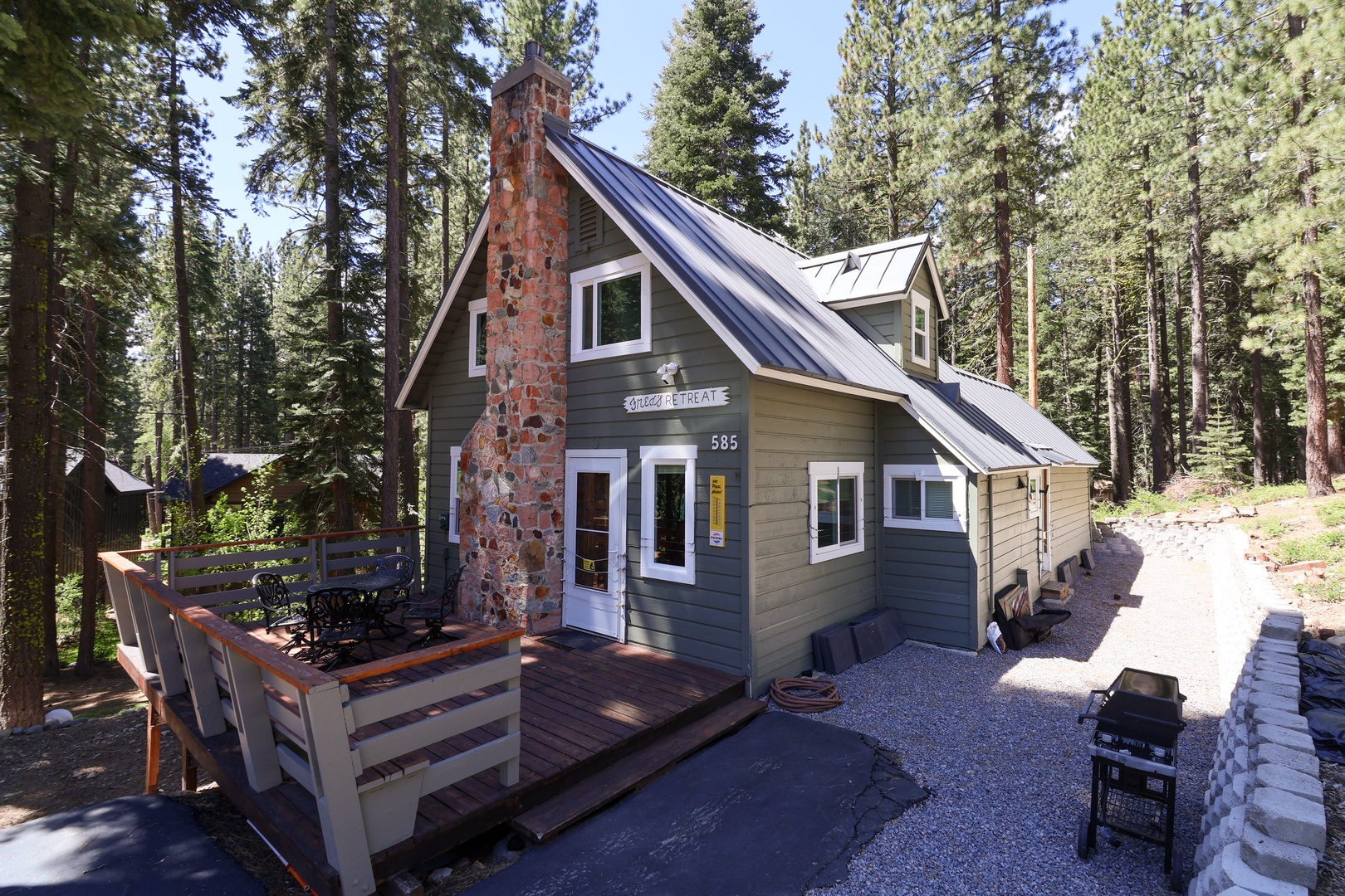 A charming A-frame cabin nestled among towering pines, featuring a stone chimney, cozy deck with seating, and convenient parking for your mountain getaway.