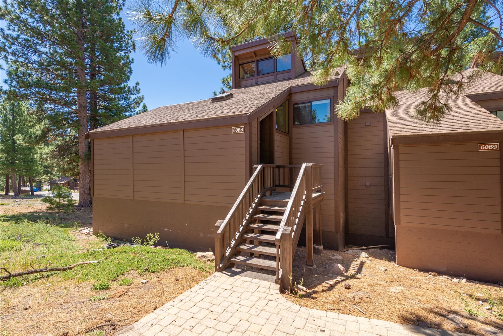 This mountain retreat features a classic wood-sided exterior with a private garage and wooden staircase leading to the front entrance, nestled among towering pines and natural landscaping.