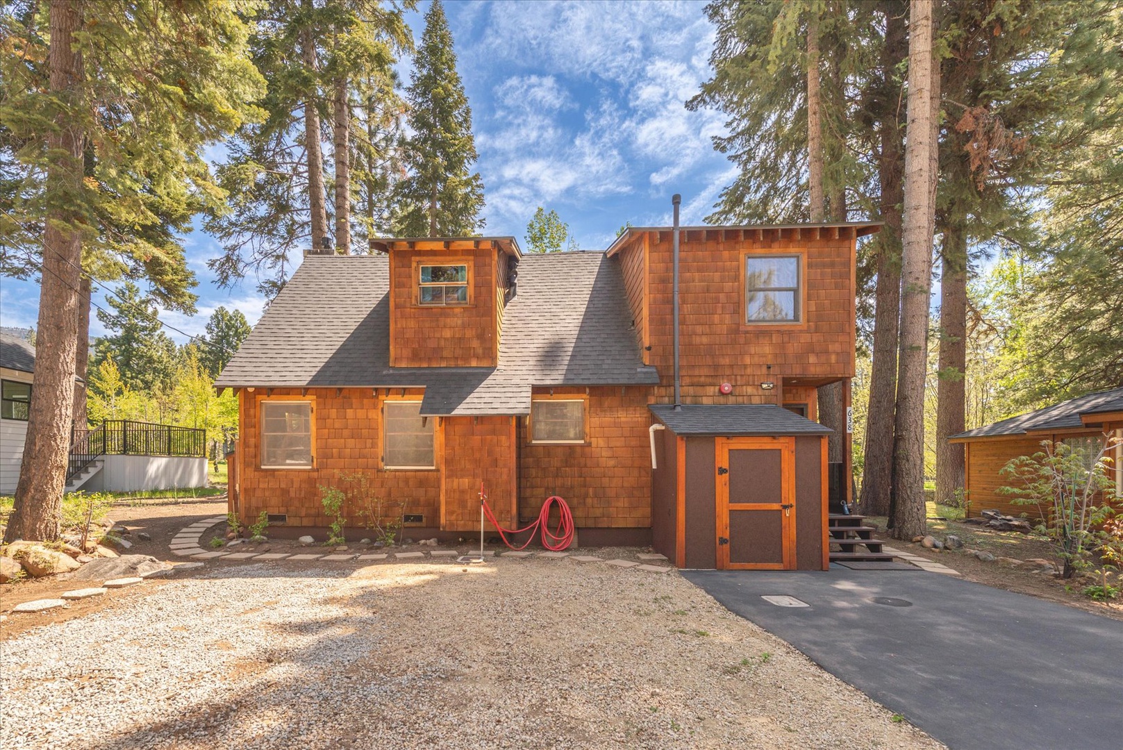 Charming cedar-shingled cabin nestled among towering pines with convenient parking and outdoor storage shed.
