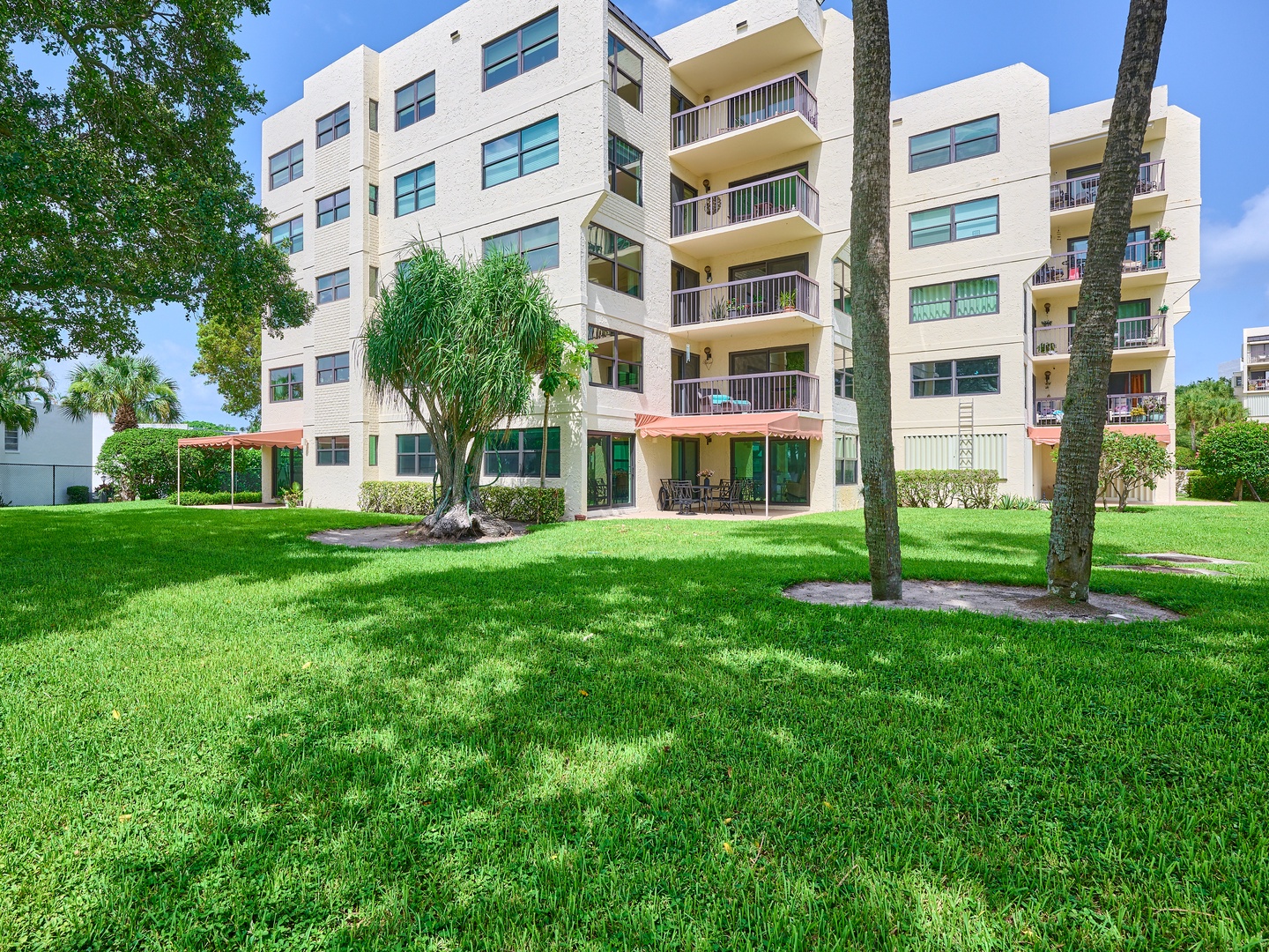 Lush tropical landscaping with mature palms and spacious lawns frame this modern Florida retreat, featuring multiple private balconies and ground-floor outdoor spaces perfect for relaxation.