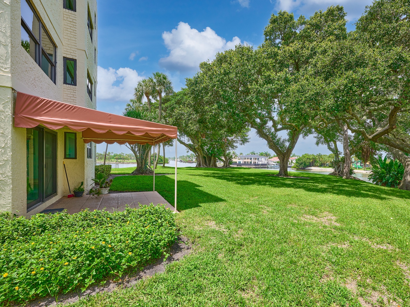 The property features a covered awning area with access to expansive green lawns shaded by mature trees, offering a peaceful outdoor setting for guests to enjoy.