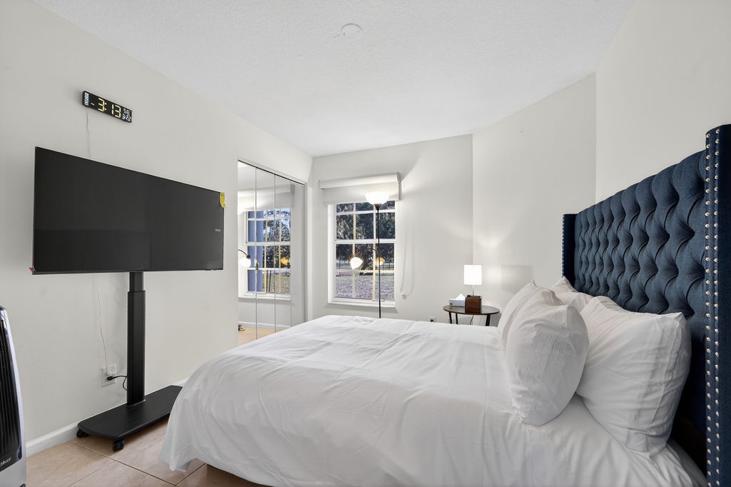 Sink into your luxurious king bed with tufted navy headboard while watching your favorite shows on the wall-mounted TV in this bright, modern bedroom.