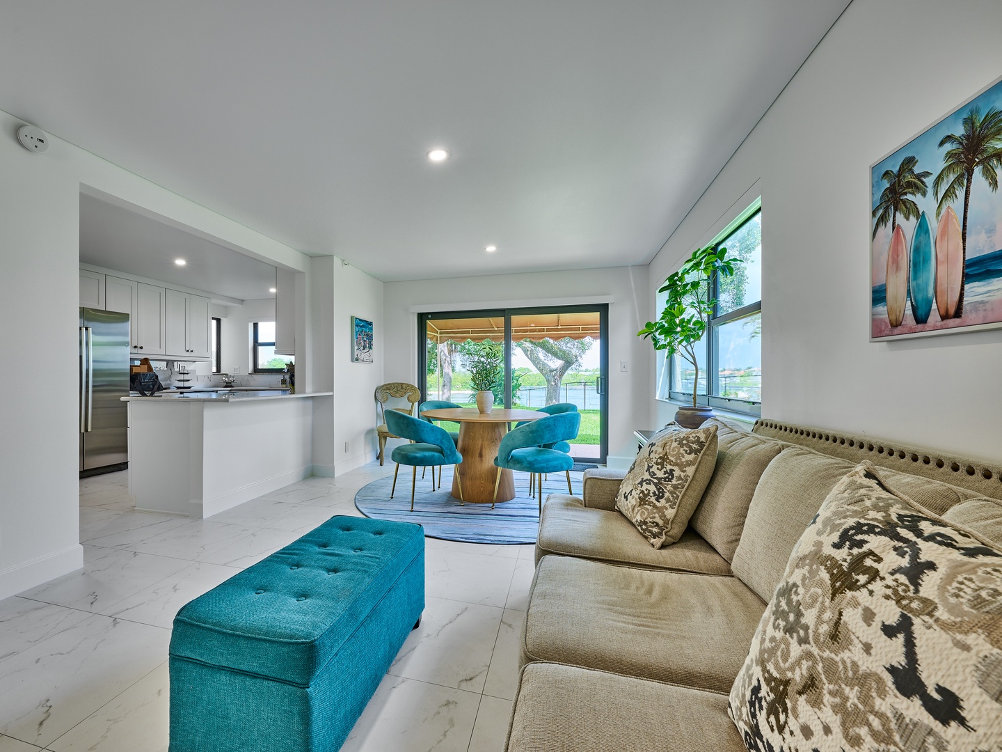 Sink into the plush sofa and let the coastal vibes wash over you—bright turquoise accents, open views of greenery, and a breezy dining nook set the perfect scene for your beach retreat.