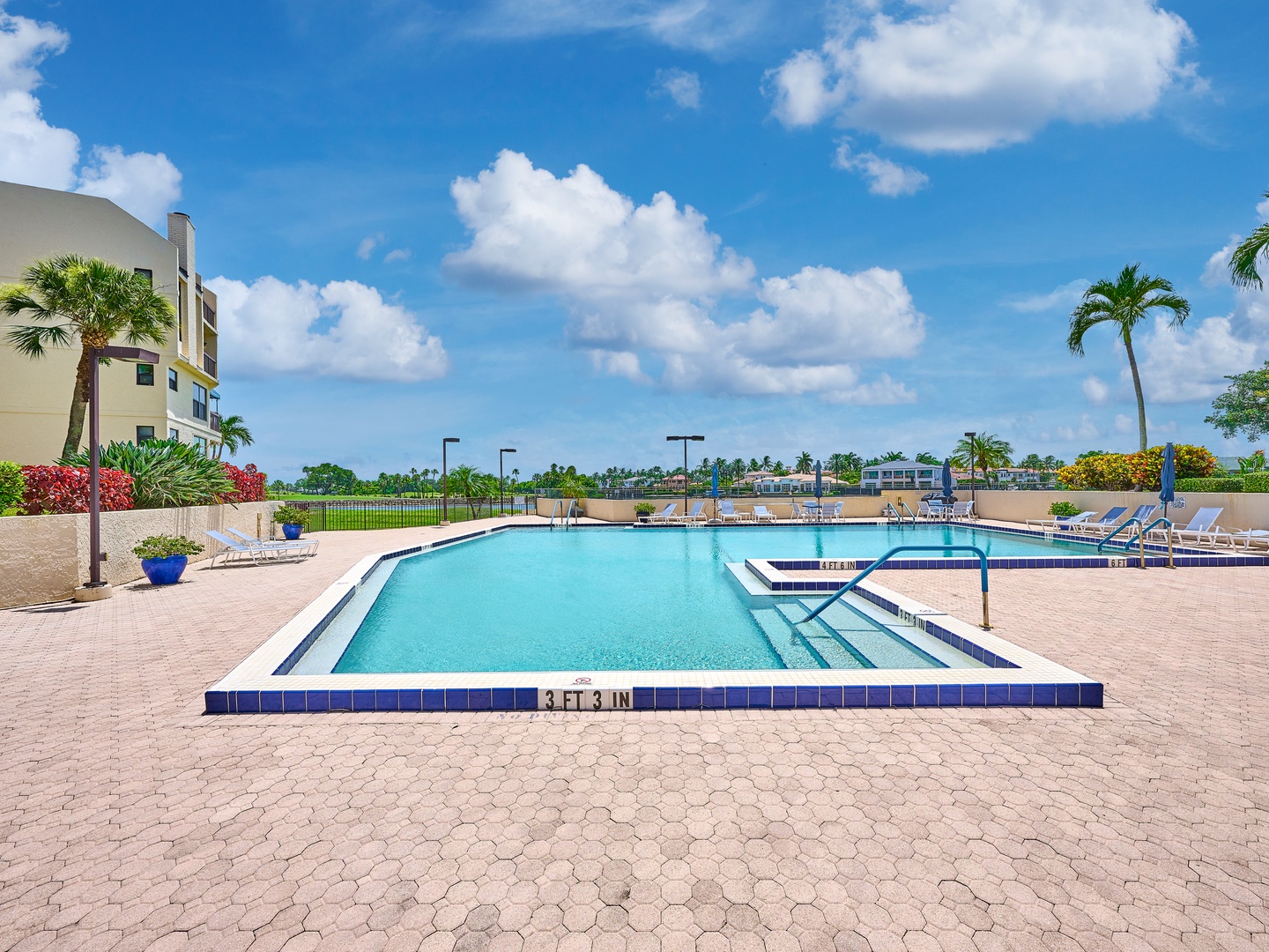 The property's sparkling pool area awaits under sunny skies, with swaying palms, loungers, and lush tropical landscaping creating a serene escape for your getaway.