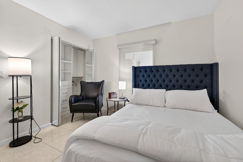 Sink into your luxurious tufted headboard bed with crisp white linens, relax in the cozy reading chair, and enjoy modern amenities in this elegant retreat.