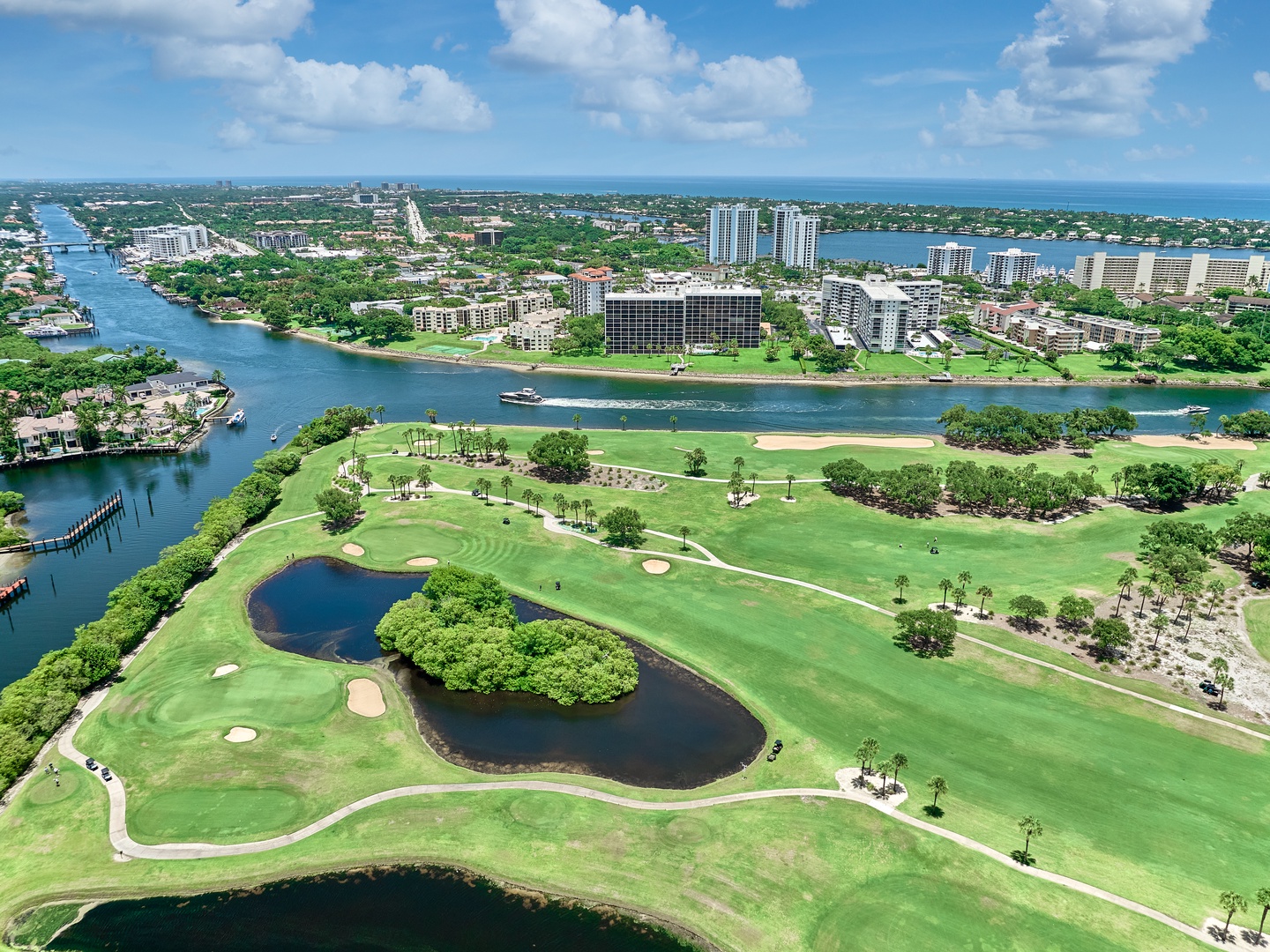 Aerial perspective showcasing the lush golf course fairways winding along the waterfront, with residential towers dotting the scenic coastal neighborhood beyond.