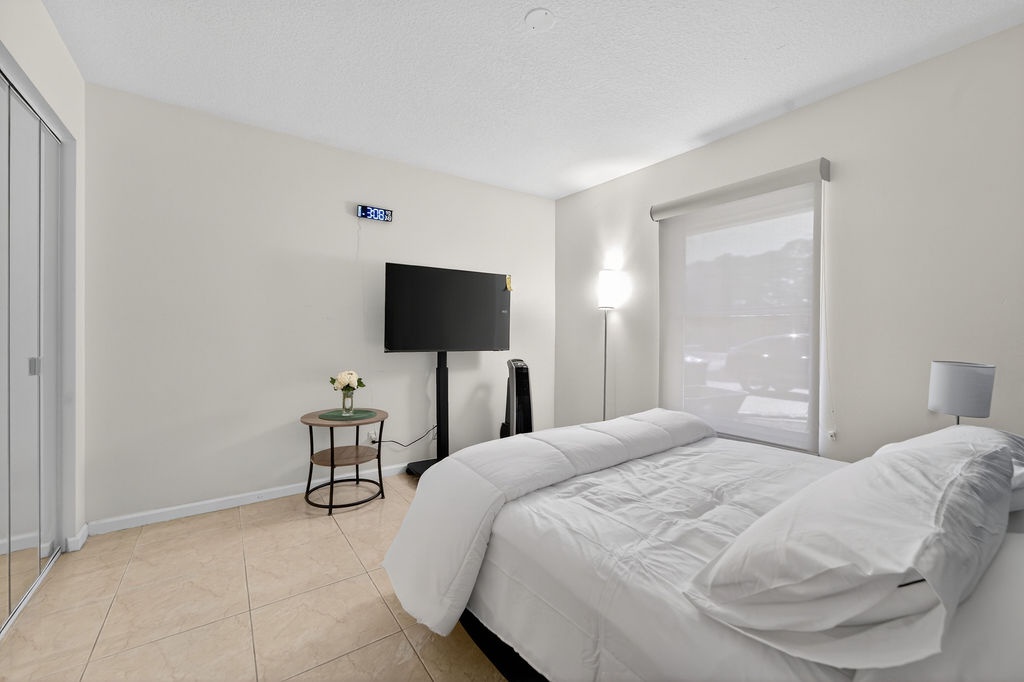 Sink into crisp white bedding in your modern bedroom, with a wall-mounted TV for evening entertainment and soft lighting creating the perfect ambiance.