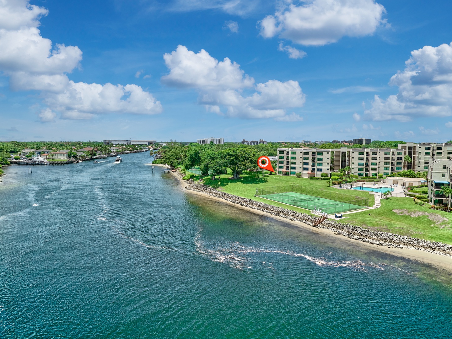 Waterfront property nestled along a serene inlet with tennis courts, lush green spaces, and a swimming pool—an idyllic coastal retreat under bright blue skies.