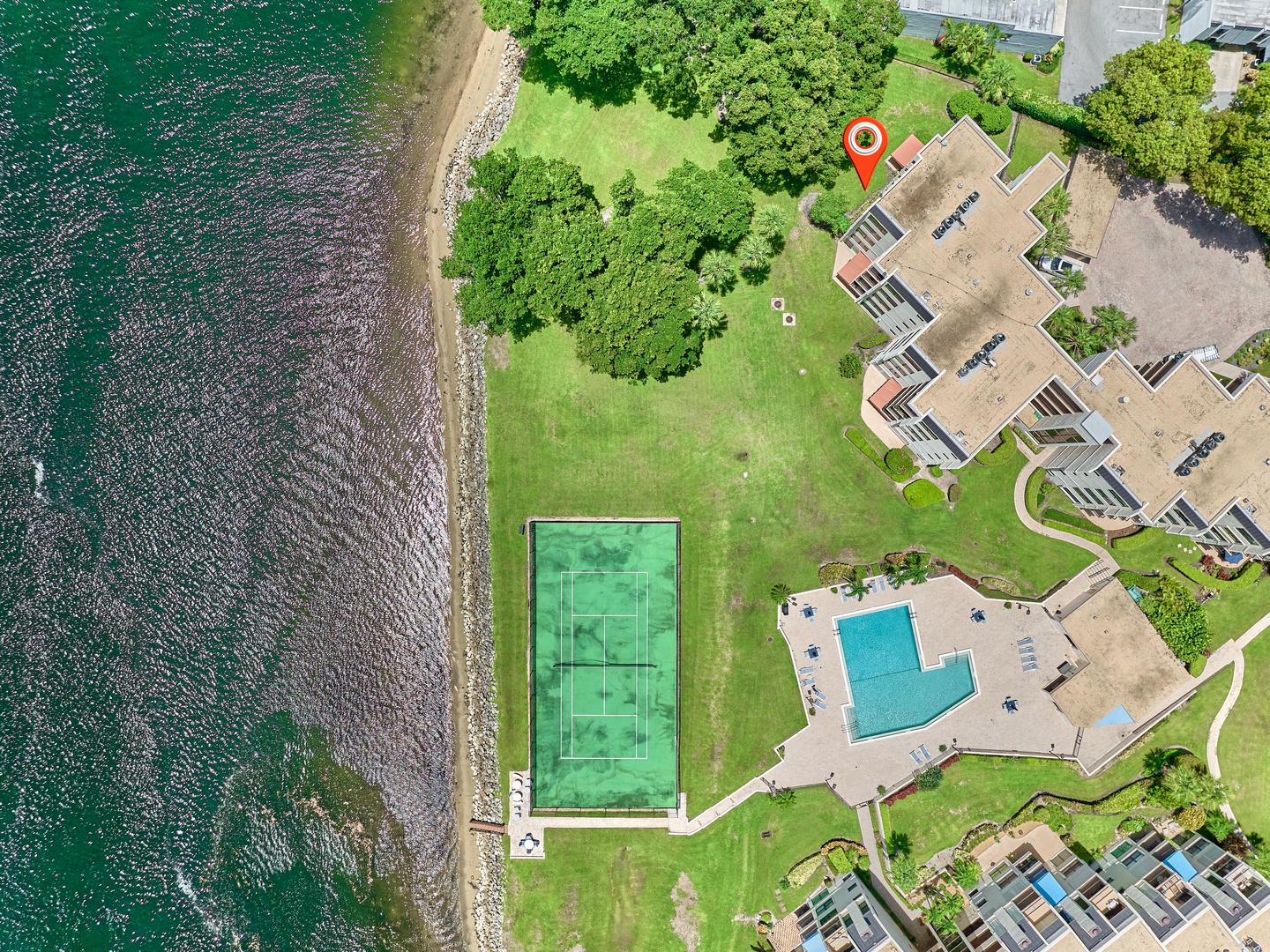 Aerial view of a waterfront property featuring a swimming pool, tennis court, and landscaped grounds with direct access to the shoreline.