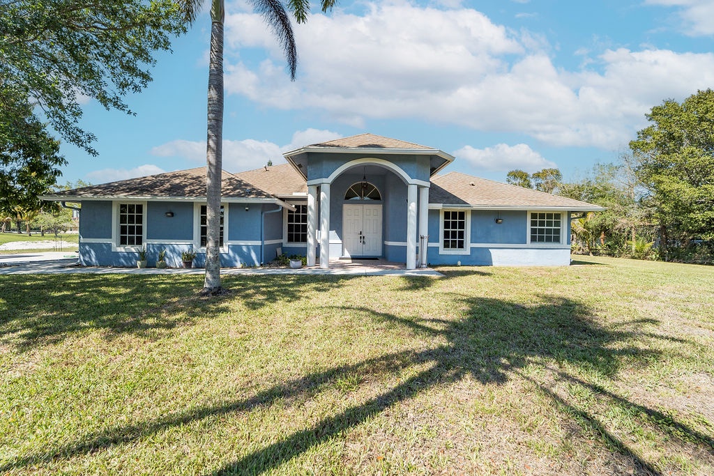 Charming blue single-story home nestled among mature palm trees and lush landscaping in a peaceful residential setting.