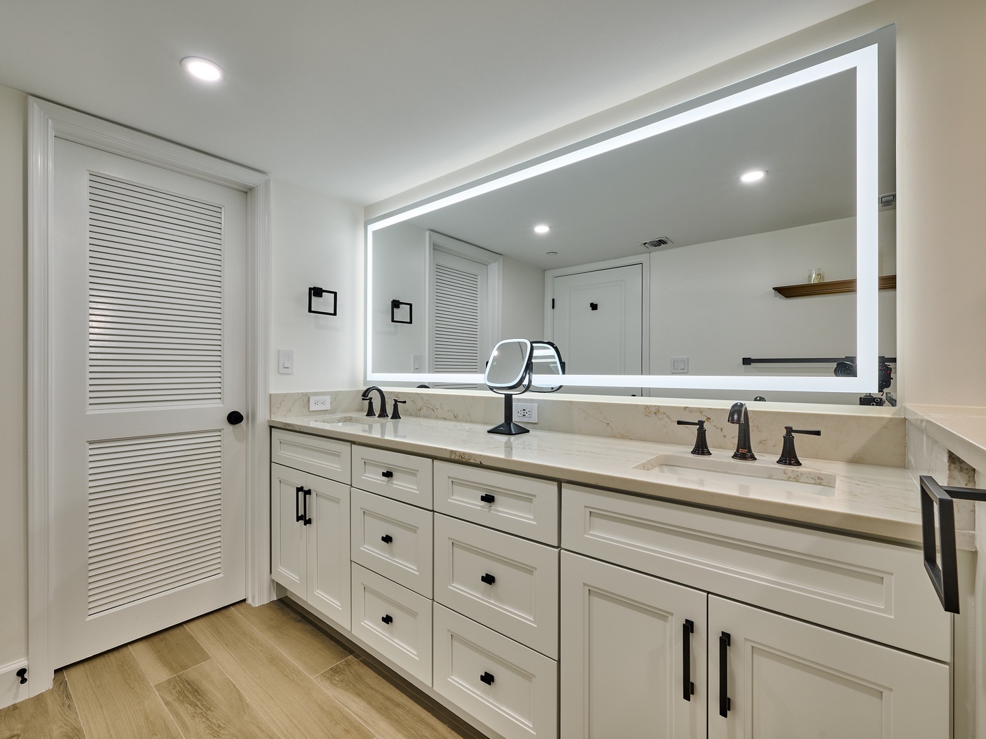 Your private bathroom features elegant dual sinks with a sleek marble countertop and modern fixtures, all lit by a bright LED mirror. Crisp white cabinetry offers abundant storage for all your essentials.