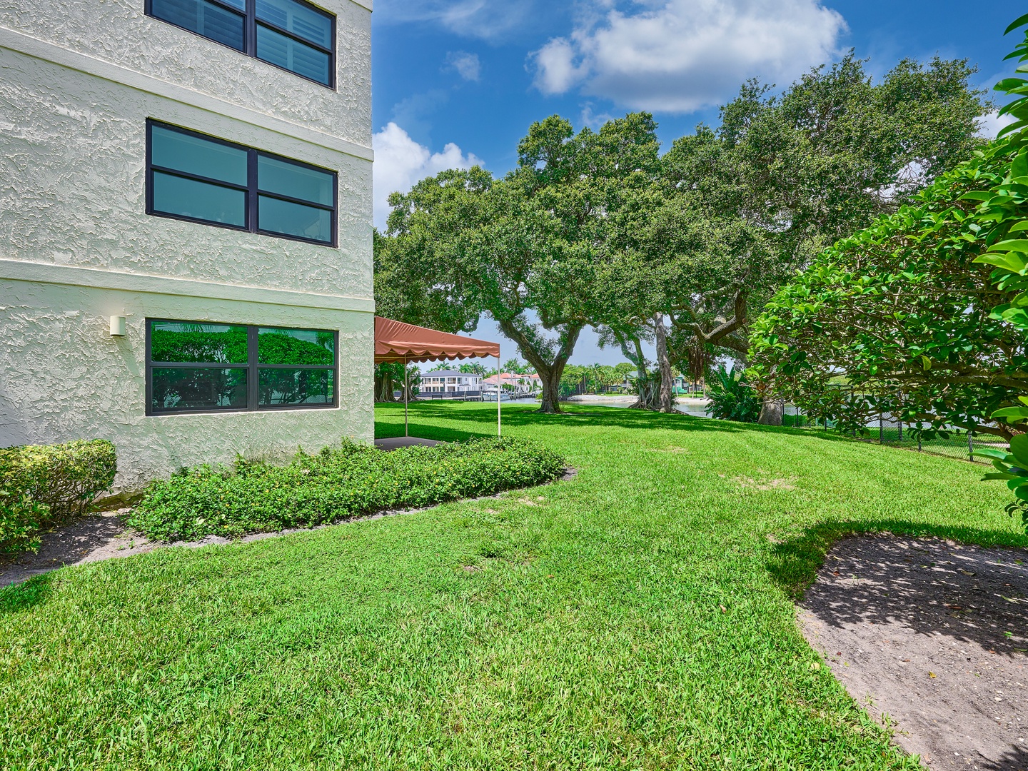 This property features lush green lawns and mature trees that create a peaceful, natural setting. The building exterior opens to inviting outdoor spaces, perfect for enjoying warm, sunny days surrounded by nature.
