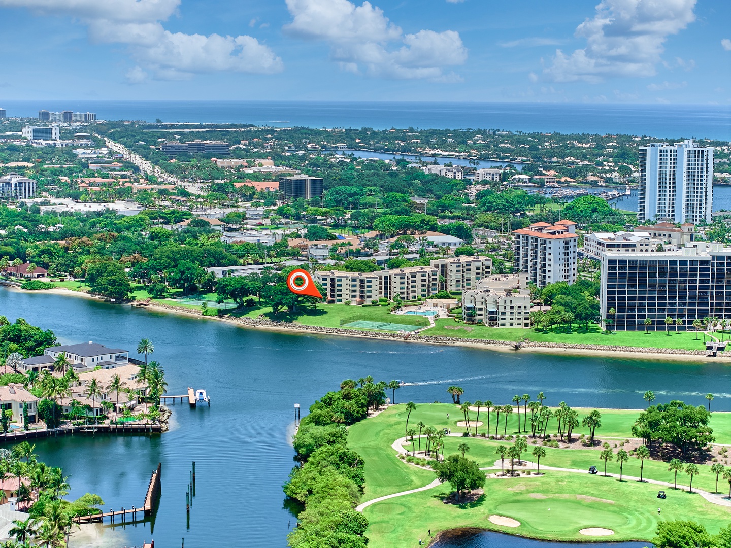 Aerial view of the property situated along scenic waterways, with golf course greens, palm-lined shores, and the blue ocean visible in the distance.
