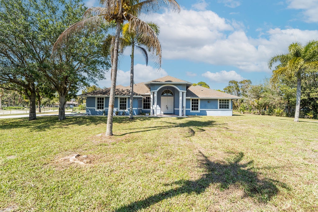 Charming blue single-story home surrounded by tropical palms and spacious lawn in a peaceful Florida neighborhood.