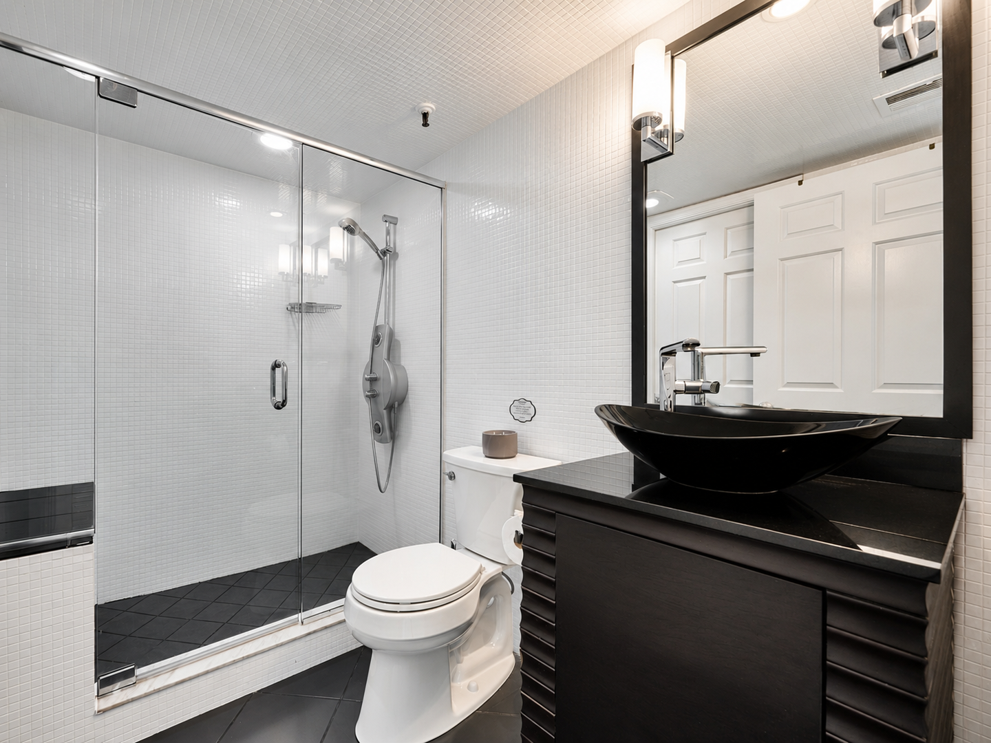 Step into your sleek, modern bathroom featuring crisp white tile, a spacious glass-enclosed shower, and a striking black vessel sink. The clean lines and contemporary design create a refreshing retreat after your day of exploring.