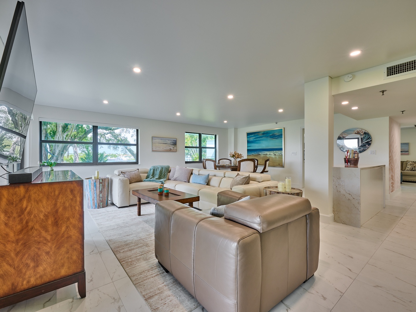Settle into this spacious, light-filled living area where comfort meets coastal elegance. Plush seating invites you to unwind while natural light streams through large windows, and art adorns the walls to inspire your stay.