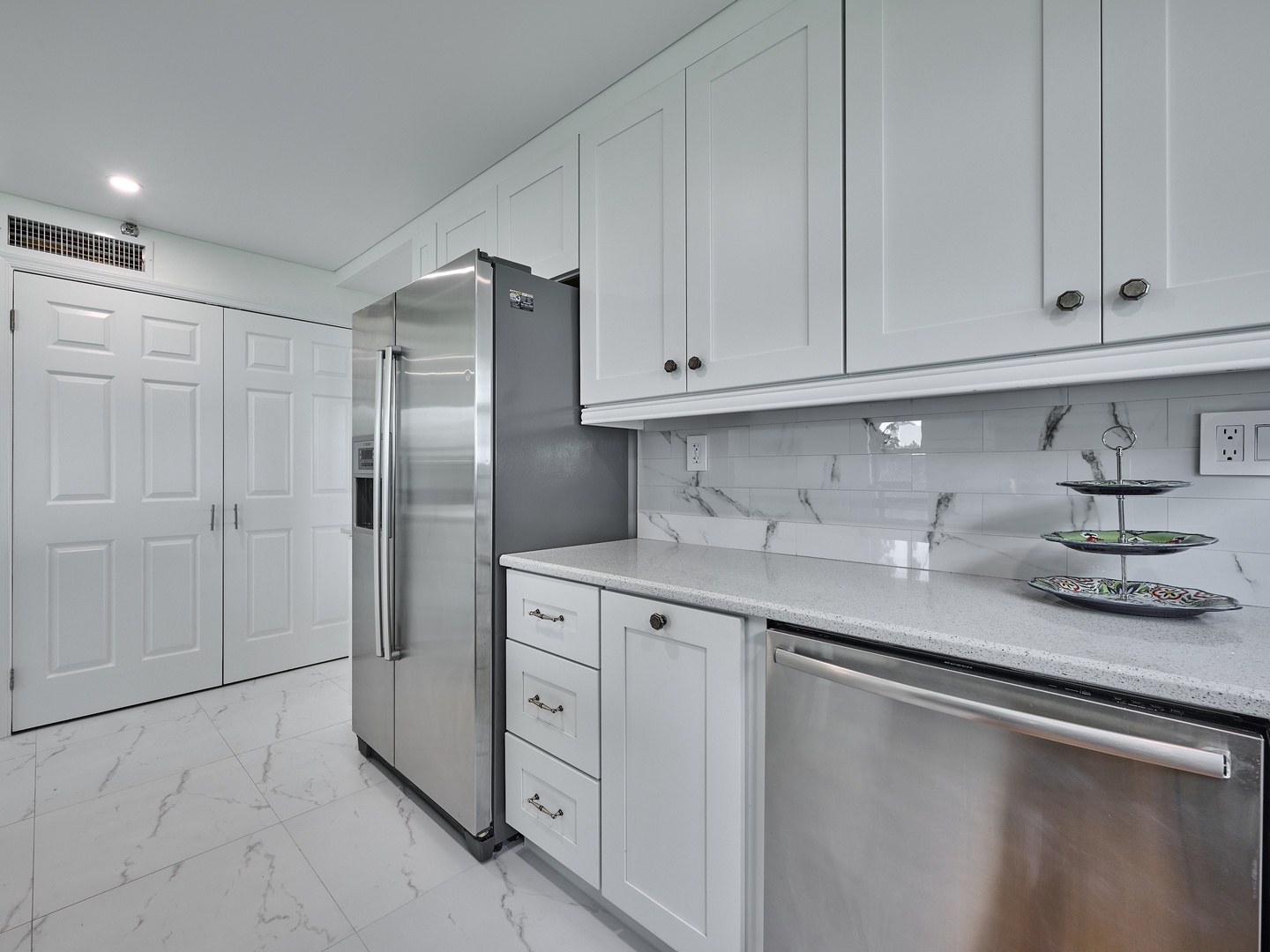 Your sleek, modern kitchen awaits with bright white cabinetry, gleaming stainless appliances, and elegant marble-look countertops—perfect for preparing meals or gathering with loved ones in style.