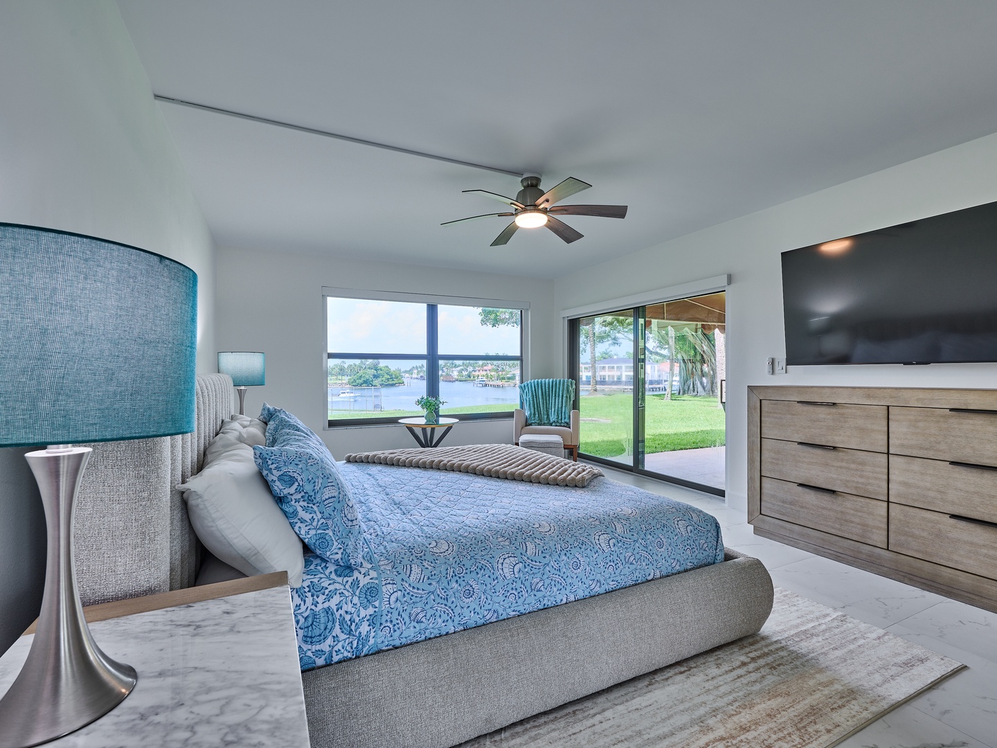 Wake up to peaceful lake views from your comfortable bed, with direct access to the outdoor patio and lush lawn beyond. Coastal-inspired linens and modern touches create a serene retreat.