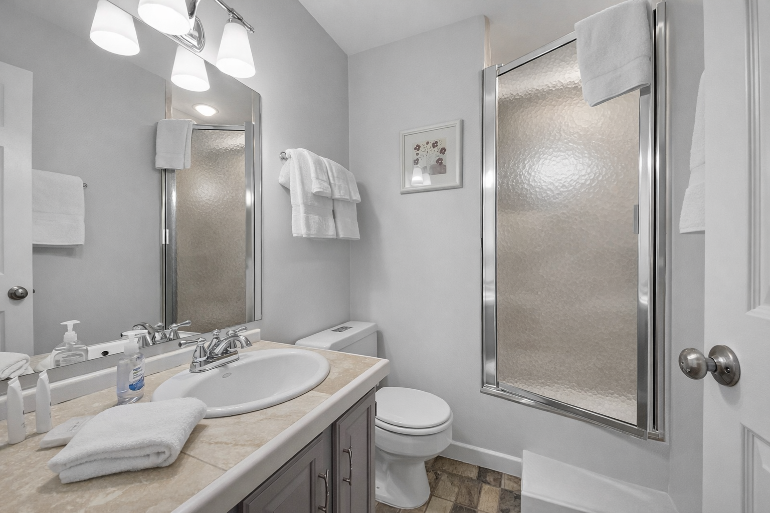 Modern & clean full bathroom featuring a sleek tub/shower combo with frosted glass door and chrome hardware. A refreshing space to unwind.