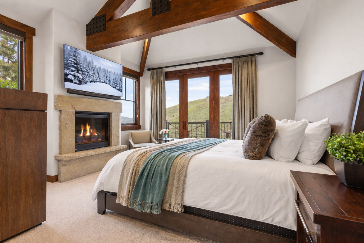 Cozy up in your mountain retreat bedroom featuring exposed beams, a crackling fireplace, and stunning valley views through French doors.