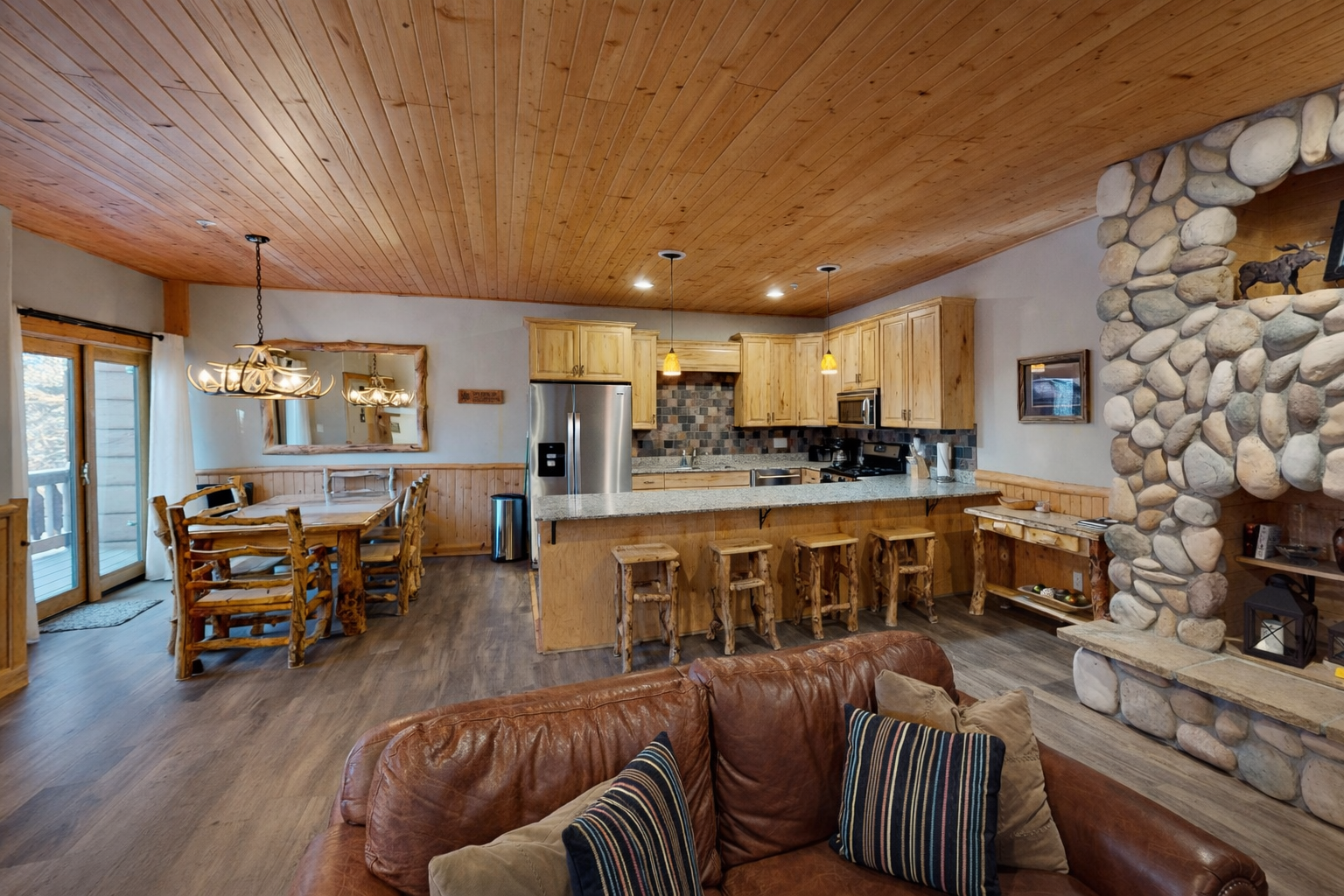 Sink into rustic luxury with your open-concept living space featuring soaring wood ceilings, a striking stone fireplace, and fully-equipped kitchen.