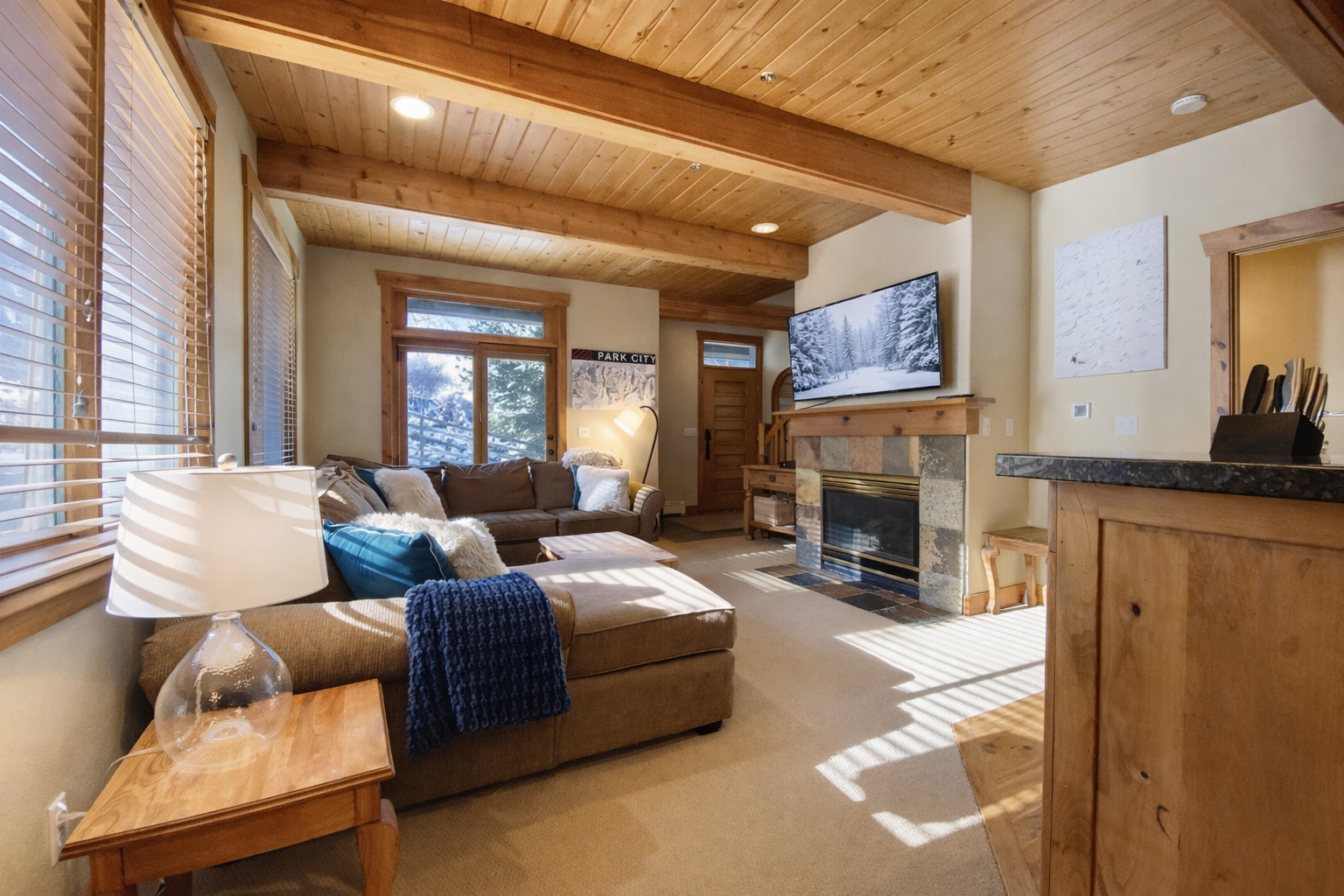 Sink into your plush sectional sofa while the fireplace crackles and natural light streams through wooden blinds in this cozy mountain retreat.