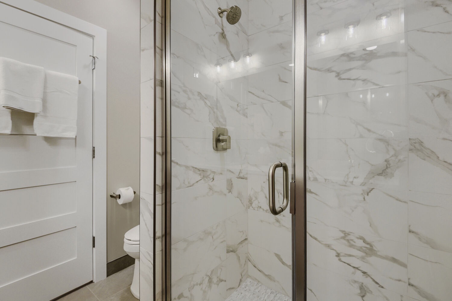 Step into your sleek glass-enclosed marble shower with elegant fixtures and a refreshing rainfall head. Crisp white towels await nearby for your comfort.