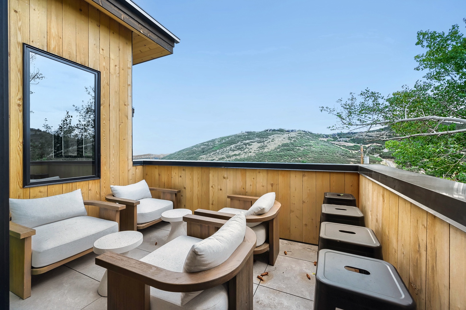 A modern mountain retreat with a private terrace overlooking rolling green hills. Natural wood finishes surround comfortable seating where you can soak in scenic vistas and breathe fresh mountain air.