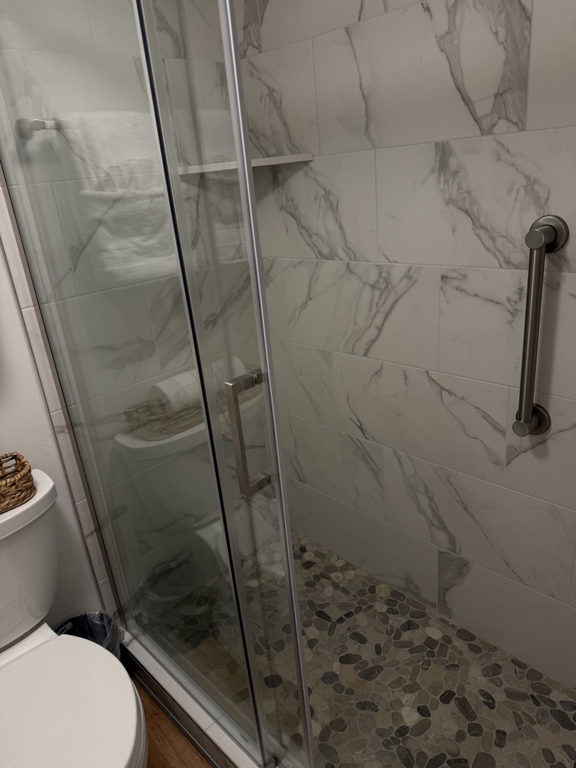 Step into your spa-like sanctuary with elegant marble-inspired tile and a sleek glass enclosure. The pebble floor adds texture and comfort while the grab bar ensures your safety and ease.
