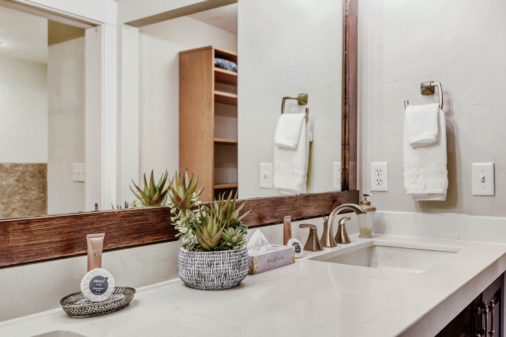 Freshen up at your spacious double vanity, styled with natural wood accents and thoughtful touches—plush towels, welcoming greenery, and all the comforts you need to feel right at home.
