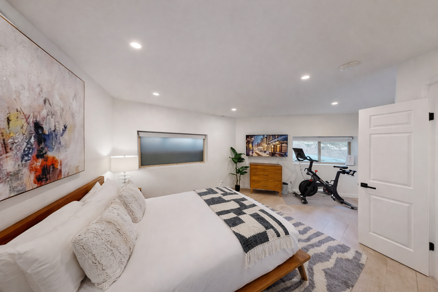 Relax in this serene, modern bedroom with a comfortable bed, ample storage, and a dedicated spin bike.