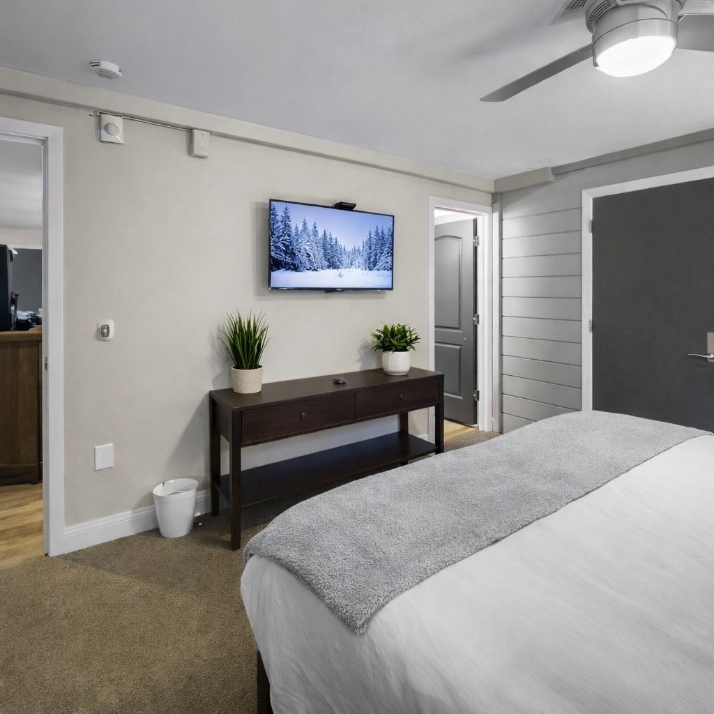 Cozy, modern bedroom featuring a plush bed with soft linens, snowy-scene smart TV, and calming décor. .