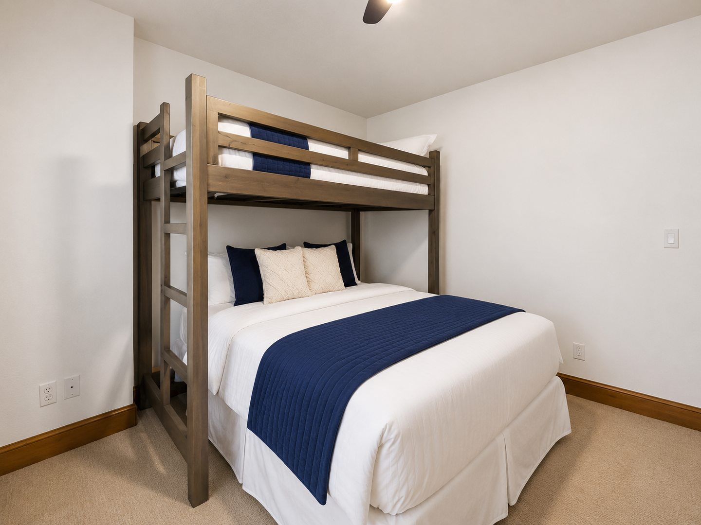 This flexible guest room features a queen bed and overhead twin bunk, perfect for families. Large windows, plush carpeting, and a cooling ceiling fan ensure a bright, comfortable stay.