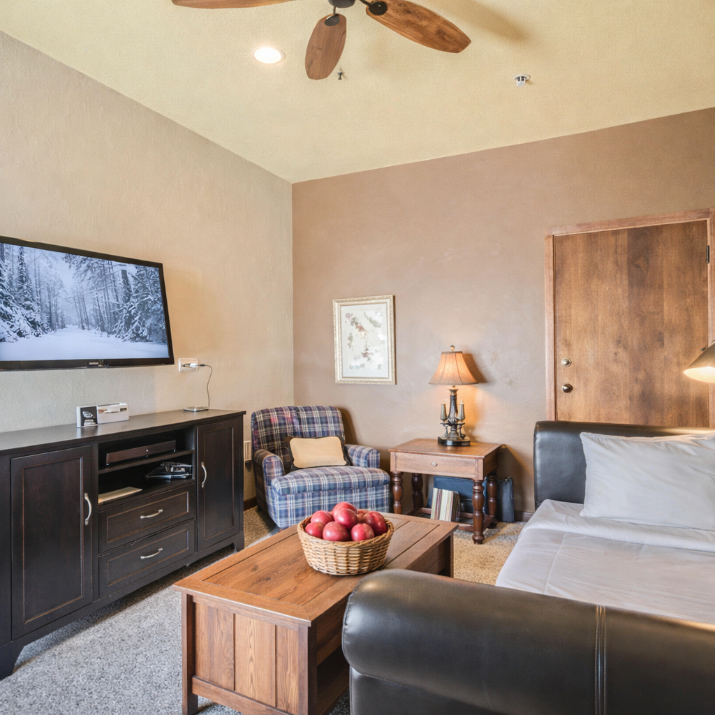 Comfortable sitting area with a sleeper sofa, plaid armchair, smart TV, and warm décor. Perfect for relaxing after exploring Park City. Features soft lighting, a rustic wood coffee table, and inviting touches.