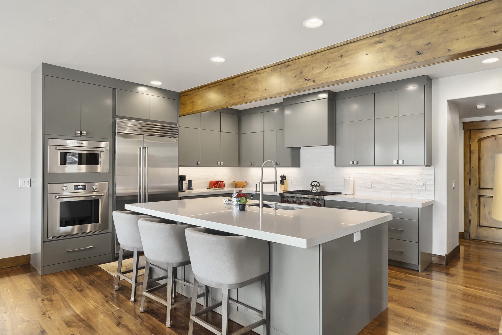 Your fully-equipped kitchen blends modern elegance with rustic charm, featuring sleek gray cabinetry, stainless steel appliances, and a spacious island perfect for preparing meals or gathering over morning coffee.