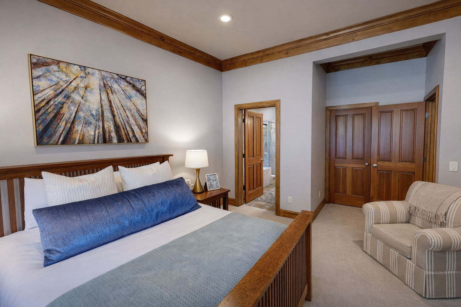 Unwind in the tranquil main floor queen bedroom. Features a plush bed, dark wood furnishings, light wood floors, and large windows with serene forest views for a peaceful stay.