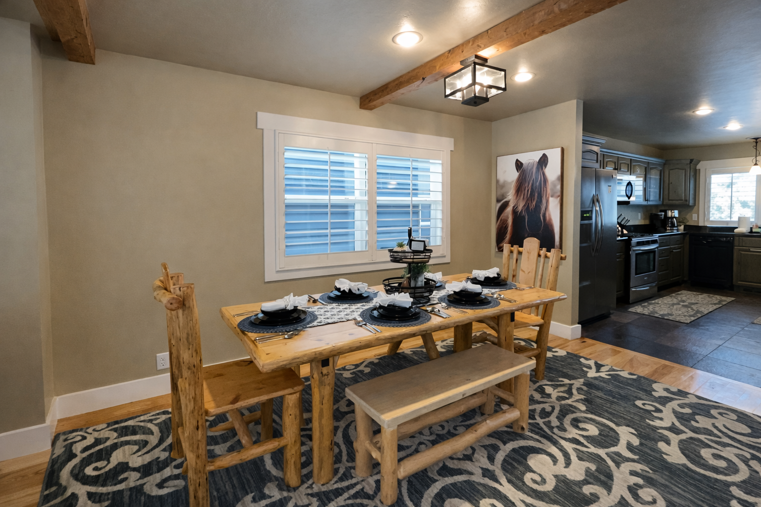 Gather around this rustic wooden dining table, featuring a mix of high-back chairs and bench seating. The space is beautifully accented with mountain-inspired decor, a patterned area rug, and soft overhead lighting.