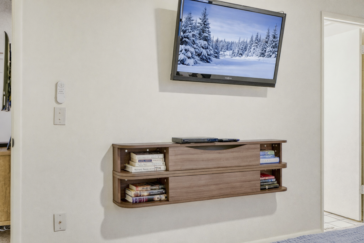 Unwind in your entertainment corner with wall-mounted TV and floating shelf filled with books for cozy evenings in.
