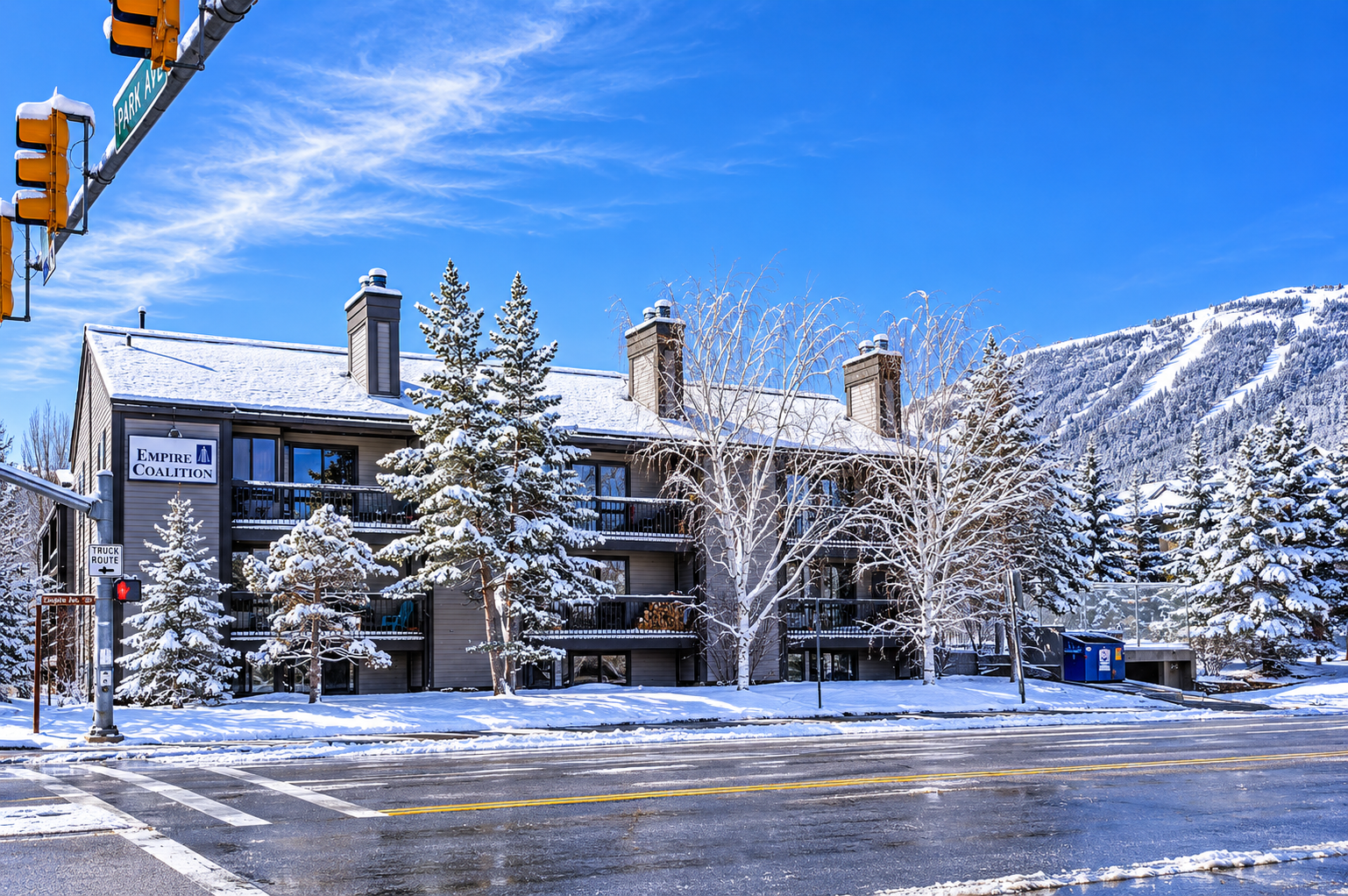 A winter wonderland awaits at Empire Coalition, nestled at the base of snow-covered slopes with frosty pines surrounding the property entrance.