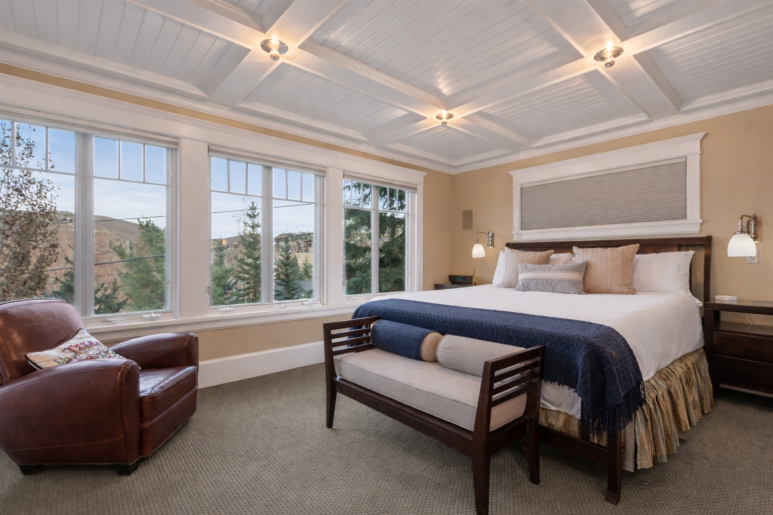 Unwind in your elegant bedroom featuring a plush bed, cozy reading chair, and stunning mountain views through expansive windows.