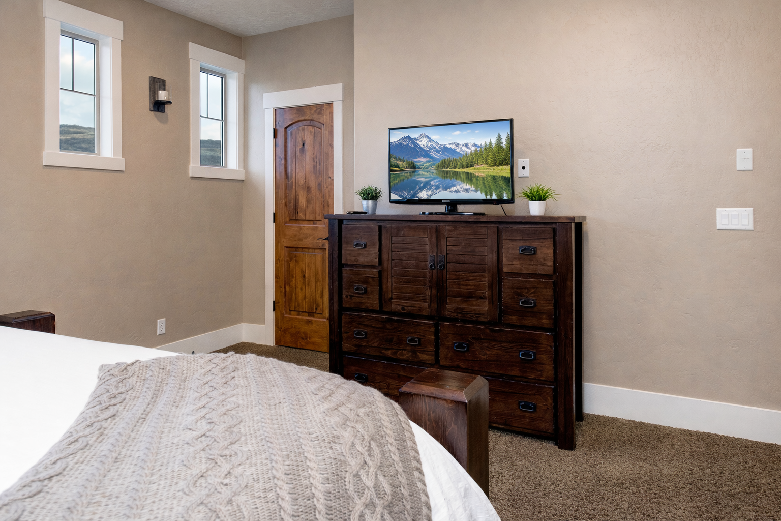 Relax in your cozy bedroom with mountain views on the TV and natural light streaming through windows overlooking peaceful countryside landscapes.