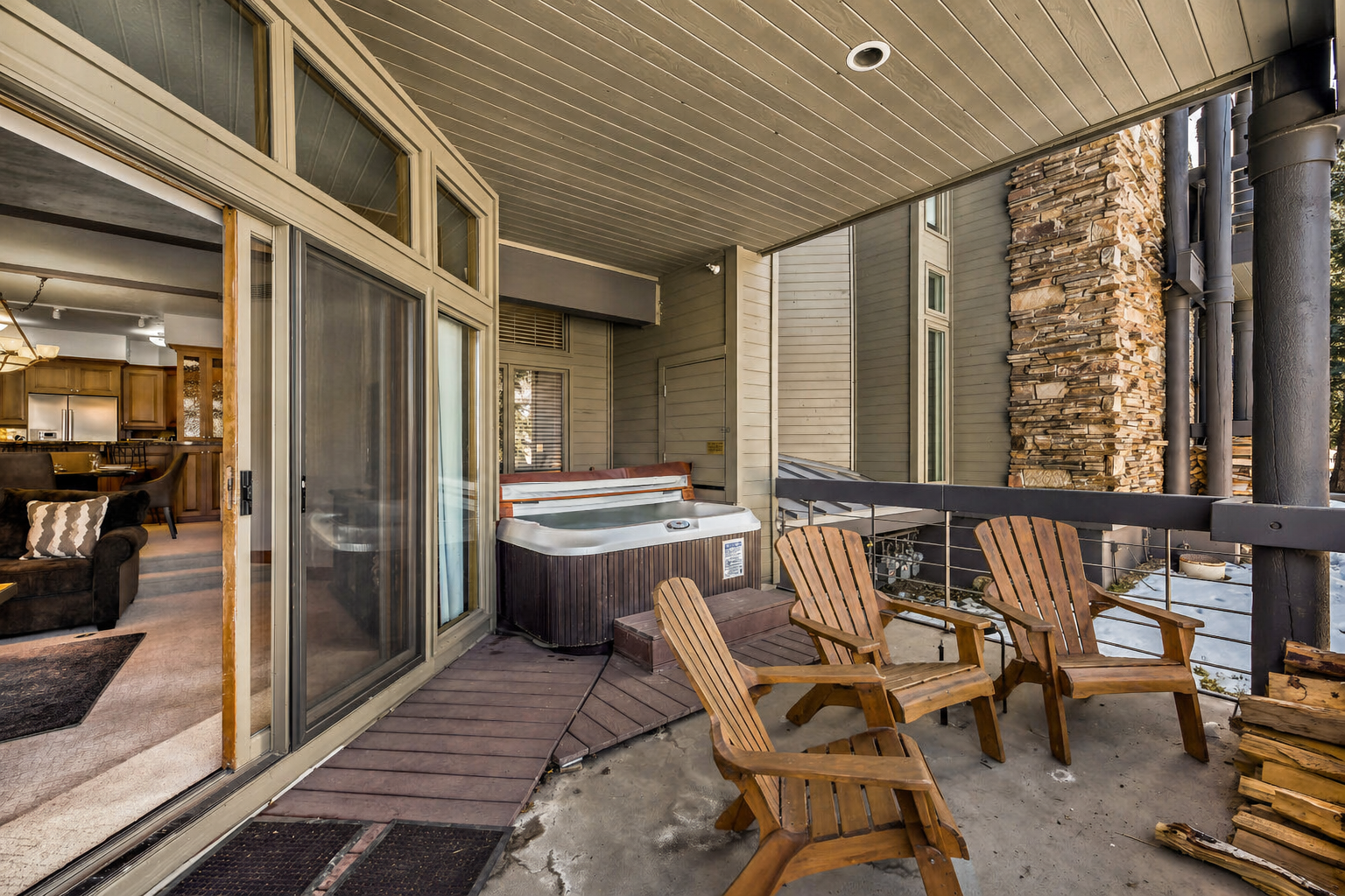 Step onto your private covered deck where relaxation awaits with comfortable wooden chairs and a bubbling hot tub, perfect for unwinding after mountain adventures.