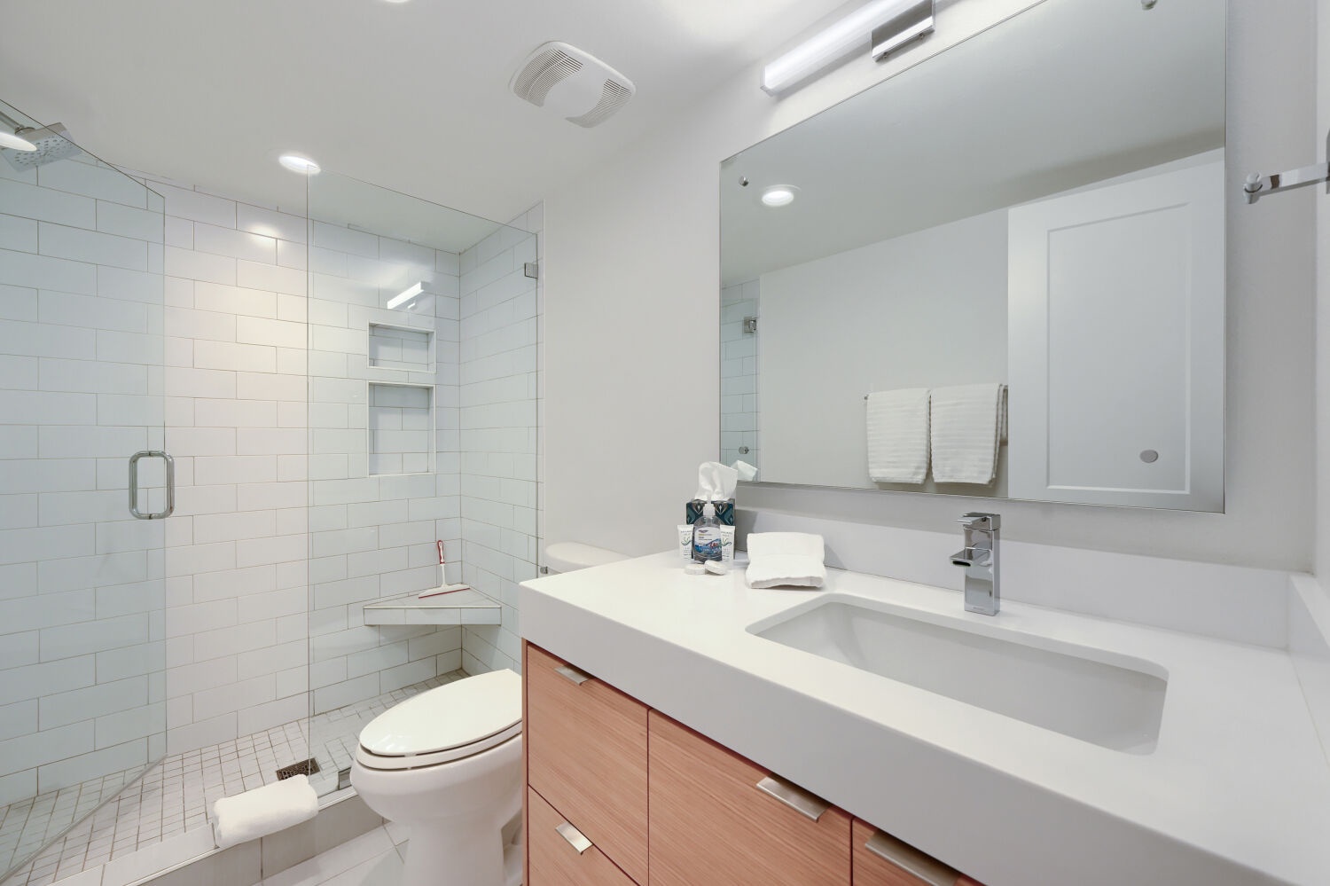 Step into your bright, modern bathroom with a spacious walk-in shower, sleek white tile, and a generous vanity. Fresh towels and thoughtful touches await you after a day of exploring.